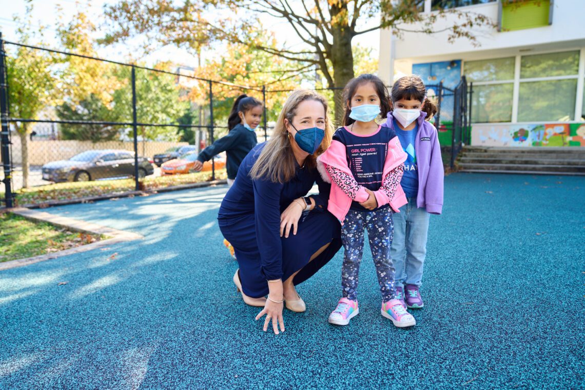 An image showing CEO Hilary Darilek with three young students on the playground, all wearing medical masks.